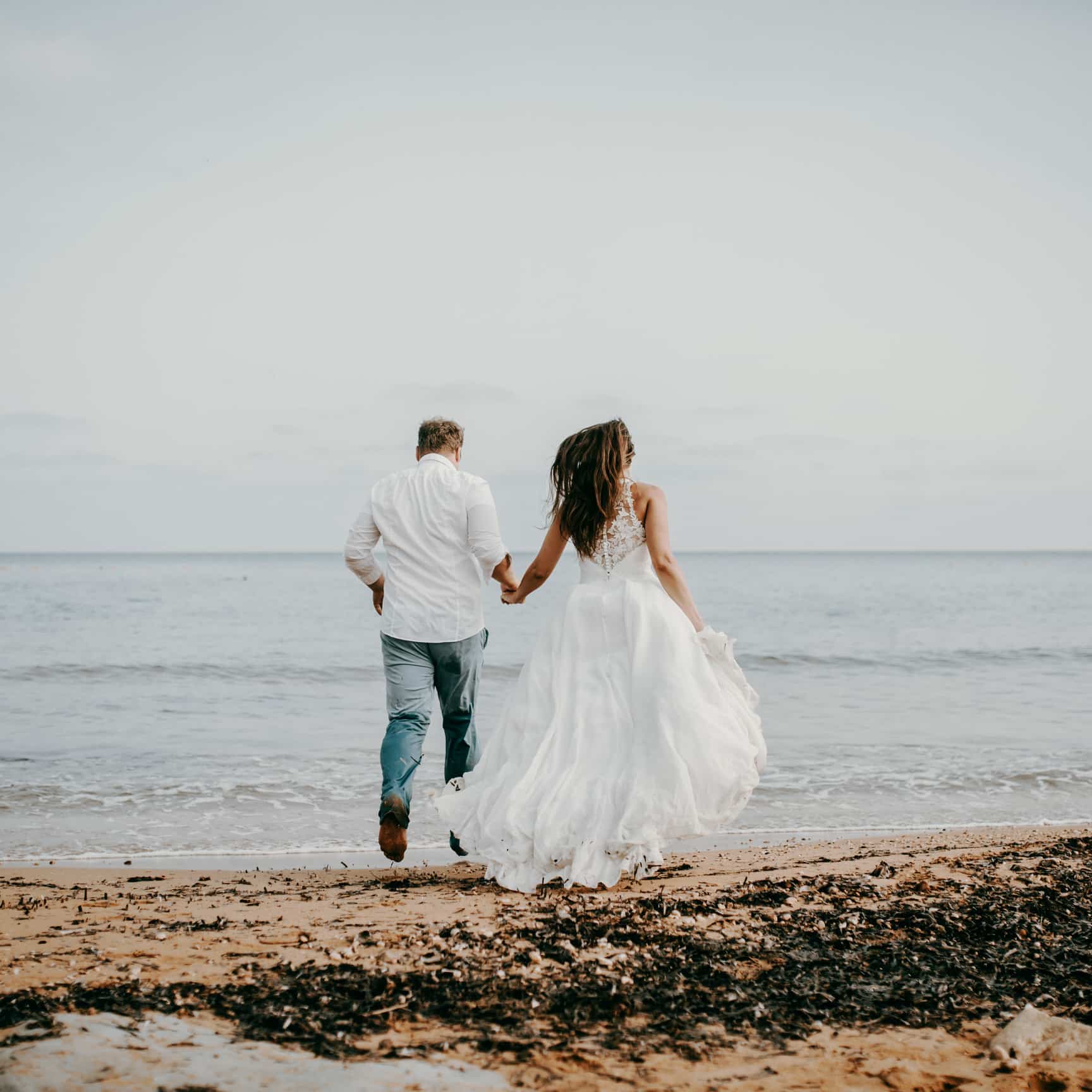 Als Hochzeitsfotograf auf Malta bei einer Strandhochzeit. Das Brautpaar rennt am Strand entlang, berührt mit den Füßen das Wasser, das Haar der Braut weht im Wind. Uns Hochzeitsfotografen Herz schlägt in solchen Momenten schneller.