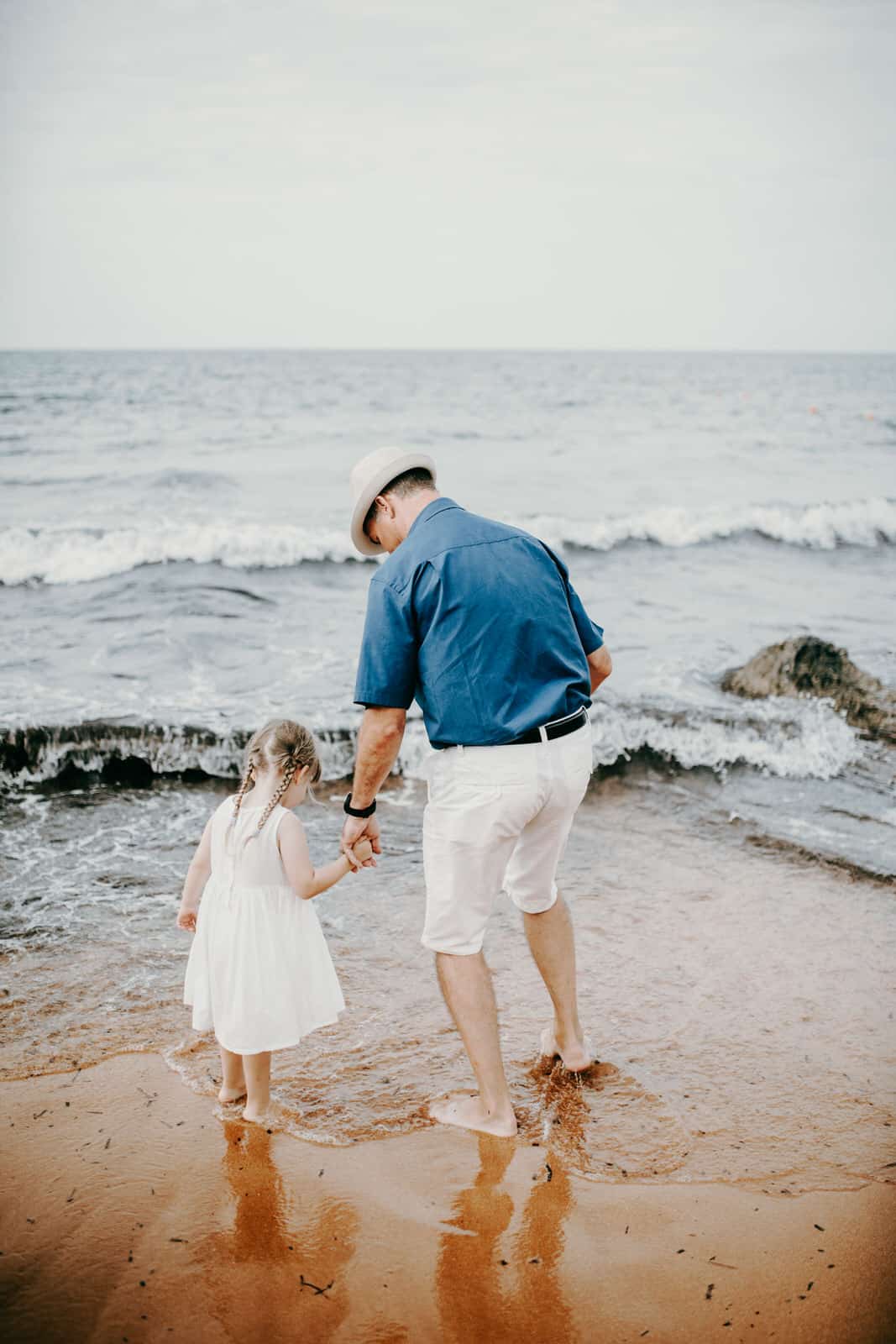 Als Hochzeitsfotograf auf Malta. Ein älterer männlicher Teilnehmer der Strandhochzeit läuft mit einem kleinen Kind an der Hand am Strand entlang. Sie sehen sich die Gischt der Wellen an. Auch das sind die wunderbaren Momente einer Hochzeit - wenn die Familie und Freunde zusammenkommen- und wir als Hochzeitsfotografen mittendrin!